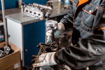 Close-up Car mechanic holding a new piston for the engine, overhaul.. Engine on a repair stand with...