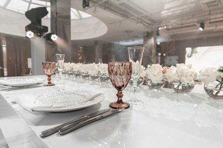 Wine glasses on round Banquet table served. Interior of restaurant for wedding dinner, ready for guests. Decorated with floral arrangement. Dishes, wine glasses and napkins. Catering concept.の写真素材