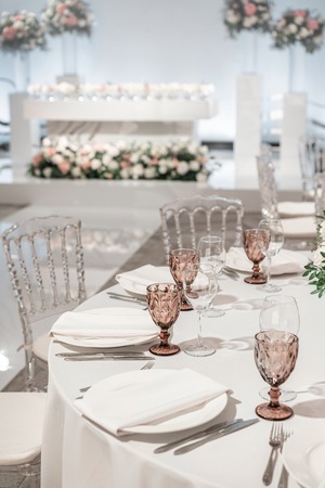 Wine glasses on round Banquet table served. Interior of restaurant for wedding dinner, ready for guests. Decorated with floral arrangement. Dishes, wine glasses and napkins. Catering concept.の写真素材