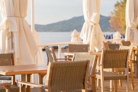 Tables in cafe. Summer sunrise on coast, Corfu island, Greece. Beach with Sunbeds and umbrellas with perfect views of the mainland Greece mountains.の写真素材