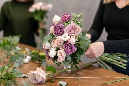 Close-up flowers in hand. Florist workplace. Woman arranging a bouquet with roses, carnation and...