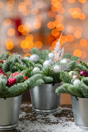 Beautiful festive set. Small arrangements of fresh spruce, pink ornamentals in a rustic wooden box. Christmas mood. Garland bokeh on background. Bokeh of Garland lights on background.の写真素材