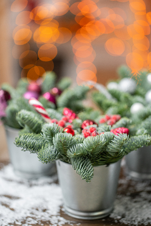 Beautiful festive set. Small arrangements of fresh spruce, pink ornamentals in a rustic wooden box. Christmas mood. Garland bokeh on background. Bokeh of Garland lights on background.の写真素材