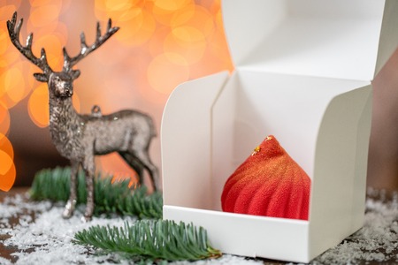 Mini mousse pastry dessert covered with red velour. Garland lamps bokeh on background. Modern european cake. French cuisine. Christmas theme. Copy spaceの写真素材