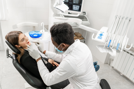 Young African male dentist with a patient. Woman in the dentist chair at dental clinic. Medicine, health, stomatology concept. dentist treating a patient.の写真素材