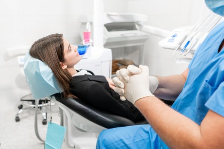 The doctor puts on rubber gloves. Doctor treats teeth. Medicine, health, stomatology concept. dentist treating a patient. . Young beautiful woman in the dentist chair at dental clinic.の写真素材
