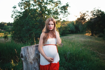 Young pregnant woman in the park outdoors. Calm pregnant woman in third trimester. Walking in public...