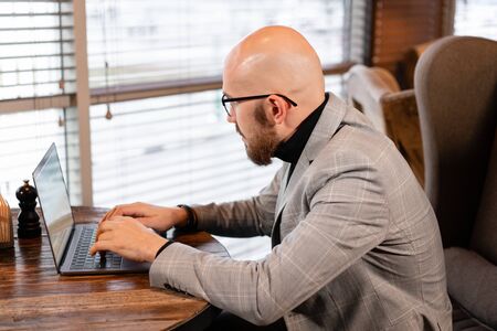 Typing on the keyboard, chatting. Young man maintains a blog. Successful people, businessman in comfortable cafe . Reading text during work on netbookの写真素材