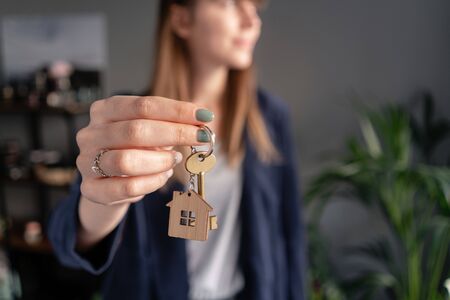 House key rotates on the finger in womans hands. Young pretty woman smiles. Modern light lobby interior. Real estate, hypothec, moving home or renting propertyの写真素材