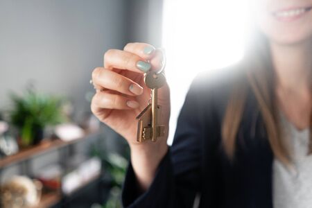 House key rotates on the finger in womans hands. Young pretty woman smiles. Modern light lobby interior. Real estate, hypothec, moving home or renting propertyの写真素材