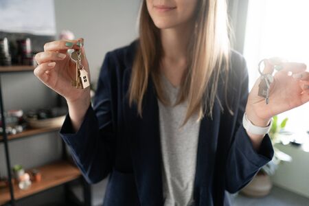 Two house keys in womans hands. Young pretty woman. Modern light lobby interior. Real estate,...