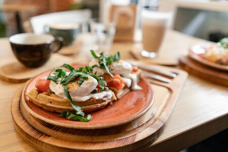 Traditional Belgian waffle with salmon, lettuce leaves and poached egg. A young woman is having Breakfast in a cafe, hands with a fork and a knife close-up.の写真素材