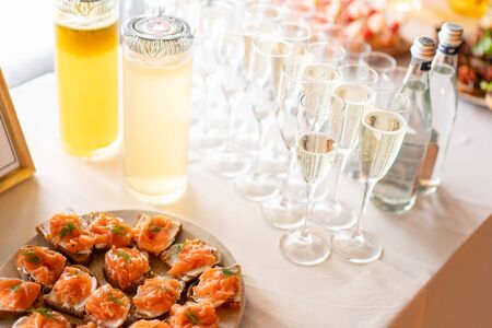 the buffet at the reception. Glasses of wine and champagne. Assortment of canapes on wooden board. Banquet service. catering food, snacks with cheese, jamon, prosciutto and fruitの写真素材