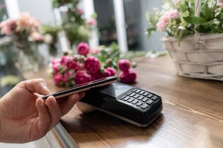 Concept contactless payment. Making payment with smartphone and pos terminal, printed check. Floral shop concept . Flowers deliveryの写真素材
