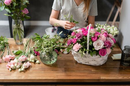 Woman florist create flower arrangement in a wicker basket. Beautiful bouquet of mixed flowers. Floral shop concept . Handsome fresh bouquet. Flowers deliveryの写真素材