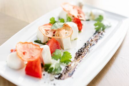 Italian traditional caprese salad. Fresh Salad with tomatoes, basil, mozzarella, and olive oil on wooden background. Mediterranean, natural and organic food concept.の写真素材