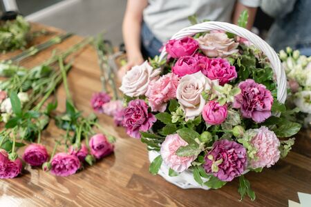 Woman florist create flower arrangement in a wicker basket. Beautiful bouquet of mixed flowers. Floral shop concept . Handsome fresh bouquet. Flowers deliveryの写真素材