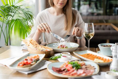 Beautiful young woman lunches in the restaurant. Tartar and a variety of dishes on the table. Italian cuisineの写真素材