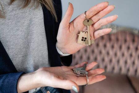 Mortgage. The concept of choice. Keys to two apartments. Young pretty woman. two house keys in womans hands. . Modern light lobby interior. Real estate, hypothec, moving home or renting property.の写真素材