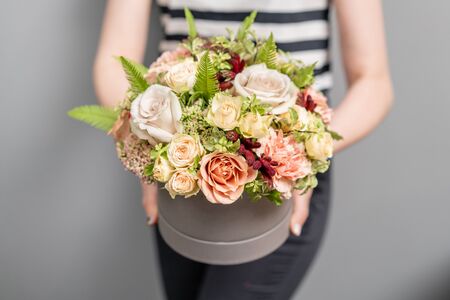 Cute little floral arrangement of mixed flowers in woman hand. Round box. The work of the florist at...
