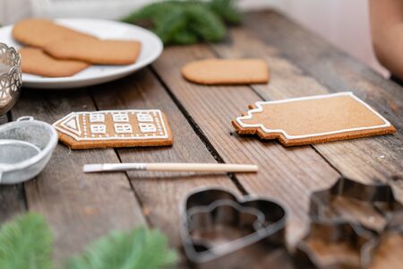 A lot of ginger biscuits in the form of European houses on brown wooden table. Decorated with white...