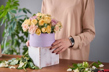 Florist woman creates flower arrangement in a round box. Beautiful bouquet of mixed flowers. Floral...