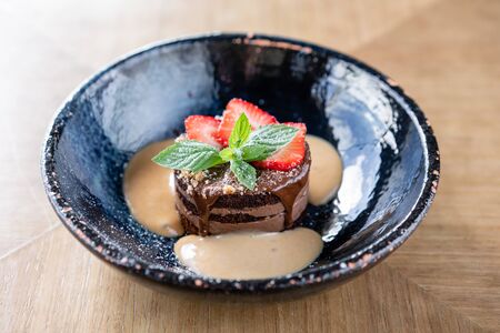 Chocolate sponge cake, with caramel, decorated with strawberries and mint leaf. Breakfast in the cafe, morning coffee. on wooden table. Restaurant menuの写真素材