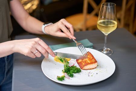 Lunch in a restaurant, a woman cuts the Salmon steak fillet and garnished with young broccoli....