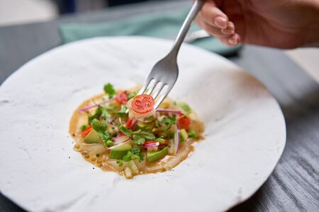 Lunch in a restaurant, a woman eat Tartar from scallop with avocado, cherry tomatoes, radishes and onion. Dish in the restaurant from raw seafood.の写真素材