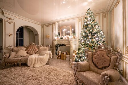 Christmas evening in the light of candles and garlands. Classic luxurious apartments with decorated christmas tree and presents. Living with fireplace, columns and stuccoの写真素材