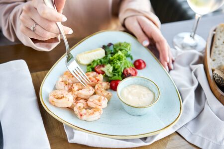 Grilled Argentine shrimp with mango-jalapeno sauce. Lunch in a restaurant, a woman eats delicious and healthy food. Delicious fresh seafood prawns with fresh vegetables and lime. Cream sauceの写真素材