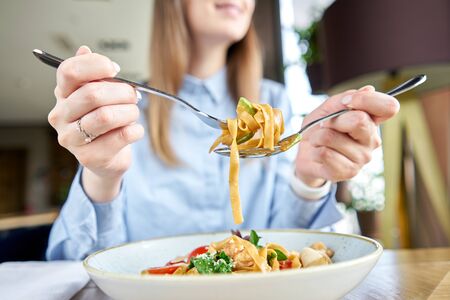 Woman eats Italian pasta with seafood and tomato sauce. Pasta Gamberini. Close-up tagliatelle wind...