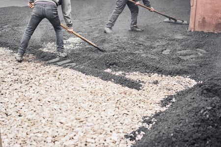 Laying new asphalt, covering the pit, on the rubble. Workers carry in shovels and using asphalt lute...