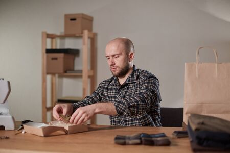 Man packs wool bow tie in box. Young man working as a tailor and using a sewing machine in workshop.