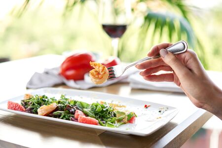 Close-up of grilled shrimps on a fork. Woman eats Delicious salad with slice grapefruit and arugula...