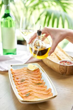 Woman pours olive oil on salted and smoked salmon or trout fillet. Thin slices of red fish with lemon close up. Restaurant menuの写真素材