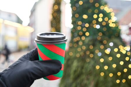 Hand holding a cup of mulled wine with blurred background of winter wonderland, a Christmas Market in European small city.の写真素材
