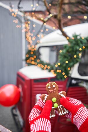 Hand in red mitten holding a smiling gingerbread man and christmas mood in blurred background....
