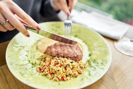 Lunch in a restaurant, a woman cuts delicious Beefsteak marbled beef, served with bulgur and smoked onion cream. Barbecue restaurant menu, a series of photos of different meats.の写真素材