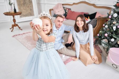 Loving family Mom and dad, little daughter . Parents and baby child having fun near Christmas tree and white fireplace indoors. Merry Christmas and Happy New Year. Cheerful pretty people.の写真素材