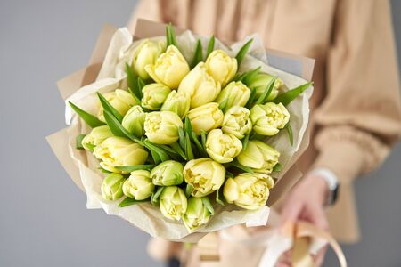 Young beautiful woman holding a spring bouquet of yellow tulips in her hand. Bunch of fresh cut spring flowers in female handsの写真素材