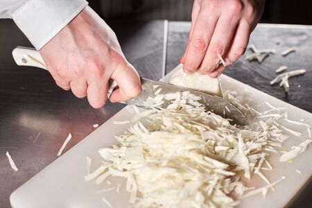 Closeup of hand with knife cutting fresh vegetable. Young chef cutting beet on a white cutting board...