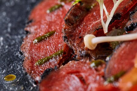 Beef carpaccio with pesto sauce and tomatoes on black table. Restaurant menu, natural and organic...