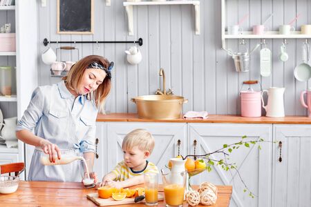 Mother and son are smiling while having a breakfast in kitchen. Mom is pouring milk into glassの素材 [FY310141922523]