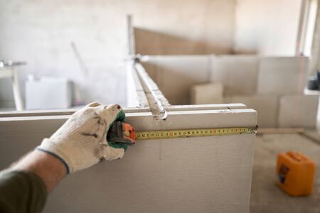 The construction worker measures with a tape measure Gypsum plate. Construction of internal walls in...