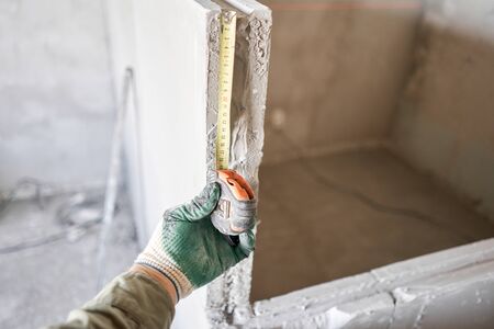 The construction worker measures with a tape measure Gypsum plate. Construction of internal walls in the apartment using a plaster concrete plate with groove ridge. tongue-and-groove gypsum blocksの写真素材
