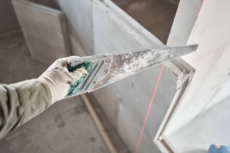 Saw in hand saws Gypsum plate. Construction of internal walls in the apartment using a plaster concrete plate with groove ridge. New building without finishing.の写真素材