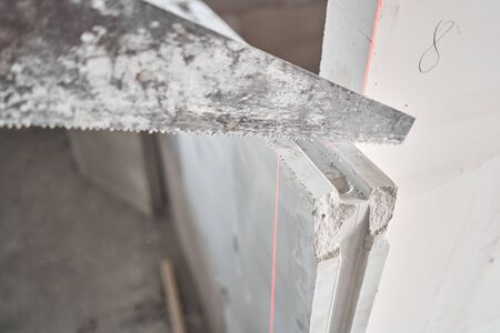 Saw in hand saws Gypsum plate. Construction of internal walls in the apartment using a plaster concrete plate with groove ridge. New building without finishing. tongue-and-groove gypsum blocksの写真素材