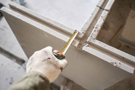 The construction worker measures with a tape measure Gypsum plate. Construction of internal walls in the apartment using a plaster concrete plate with groove ridge. tongue-and-groove gypsum blocksの写真素材