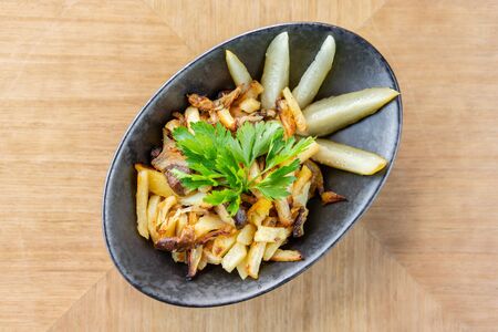 Roasted Potato country style with pickled cucumber in black bowl on wooden backgroundの写真素材